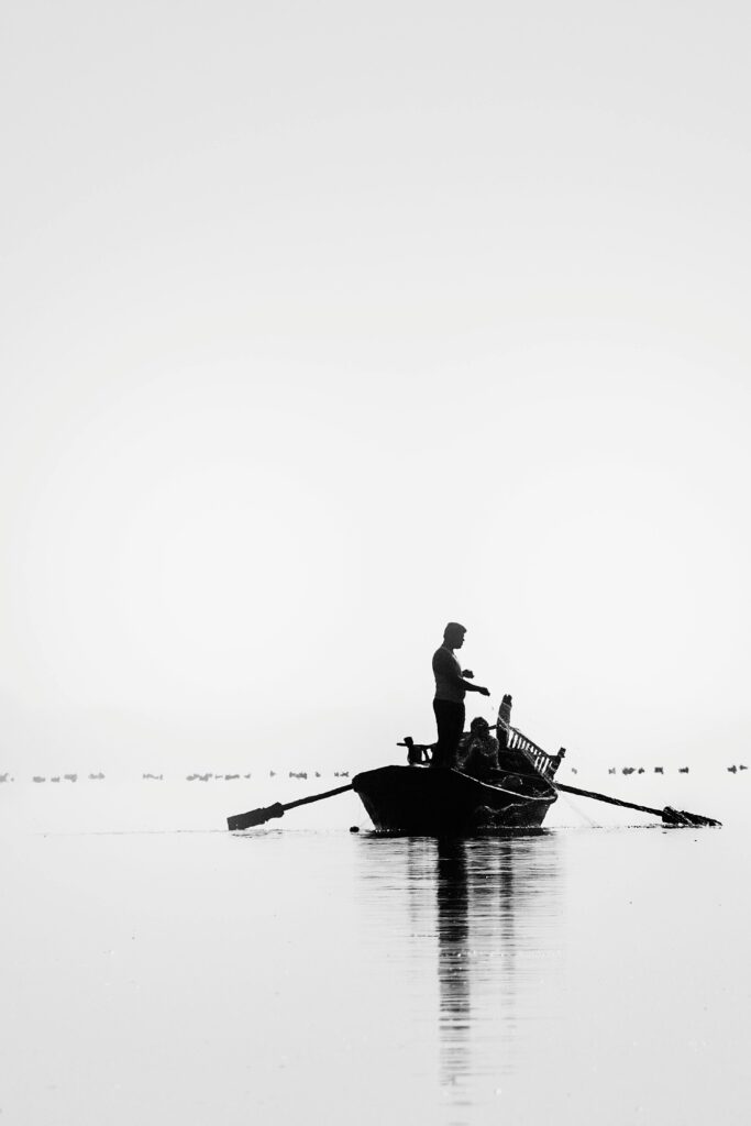 Monochromatic image capturing a lone fisherman in a boat on calm waters, creating a serene silhouette.